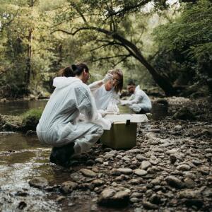 Three scientists taking water samples by a river