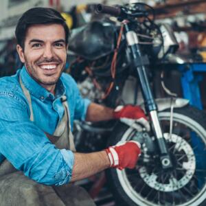 Young man smiling at camera while working on motorcycle